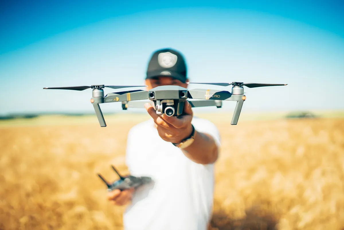 Operator holding a camera drone in front of an open field under a clear sky