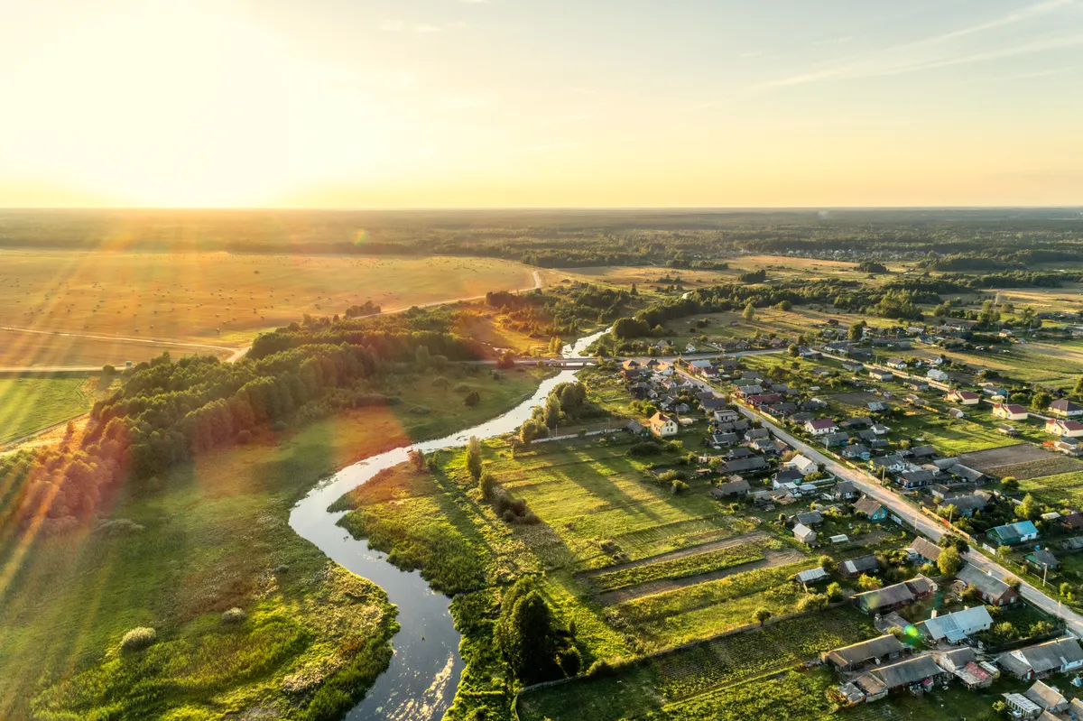 Aerial view of a small village beside a winding river at golden hour, fields and rooftops in warm light