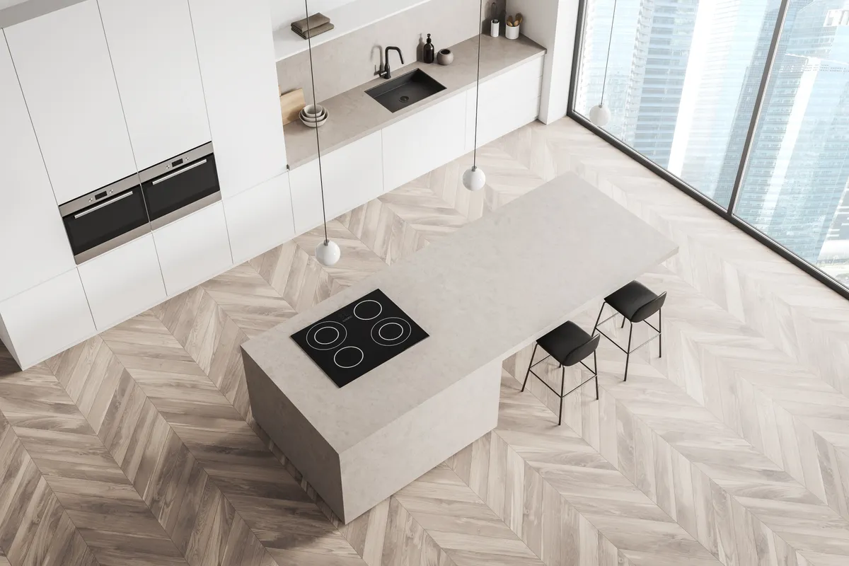 Overhead view of a minimal kitchen with a stone island, black stools and herringbone timber flooring